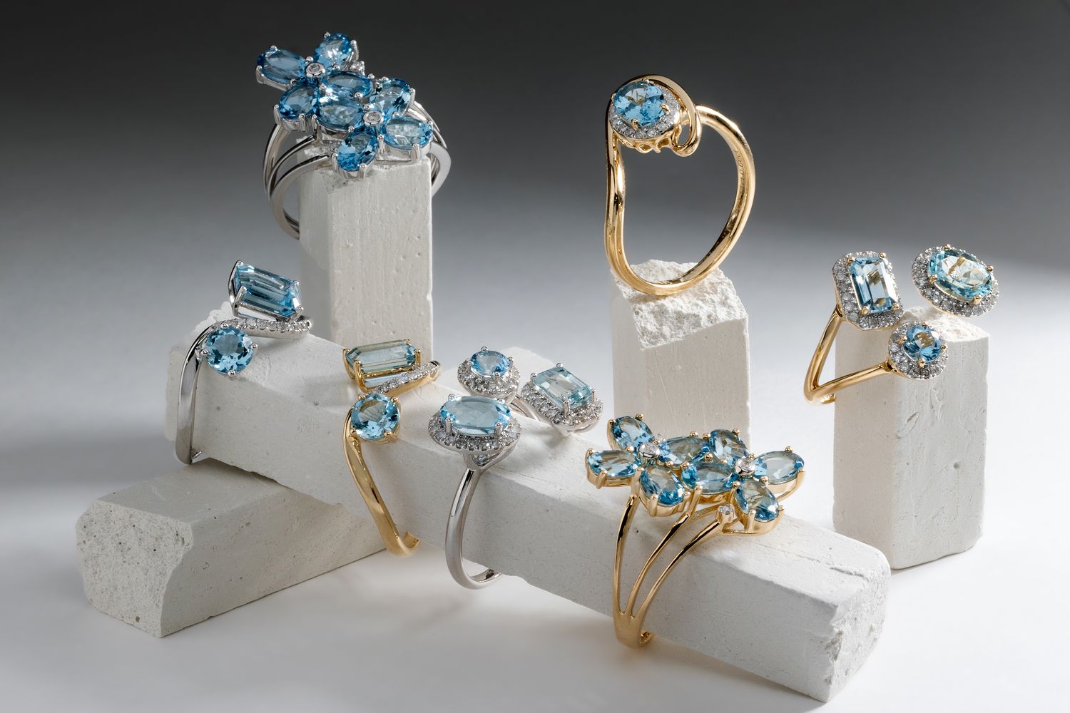 Mehrere Ringe aus Gelb- und Weißgold, besetzt mit hellblauen Edelsteinen ausgestellt auf Podesten aus Gips