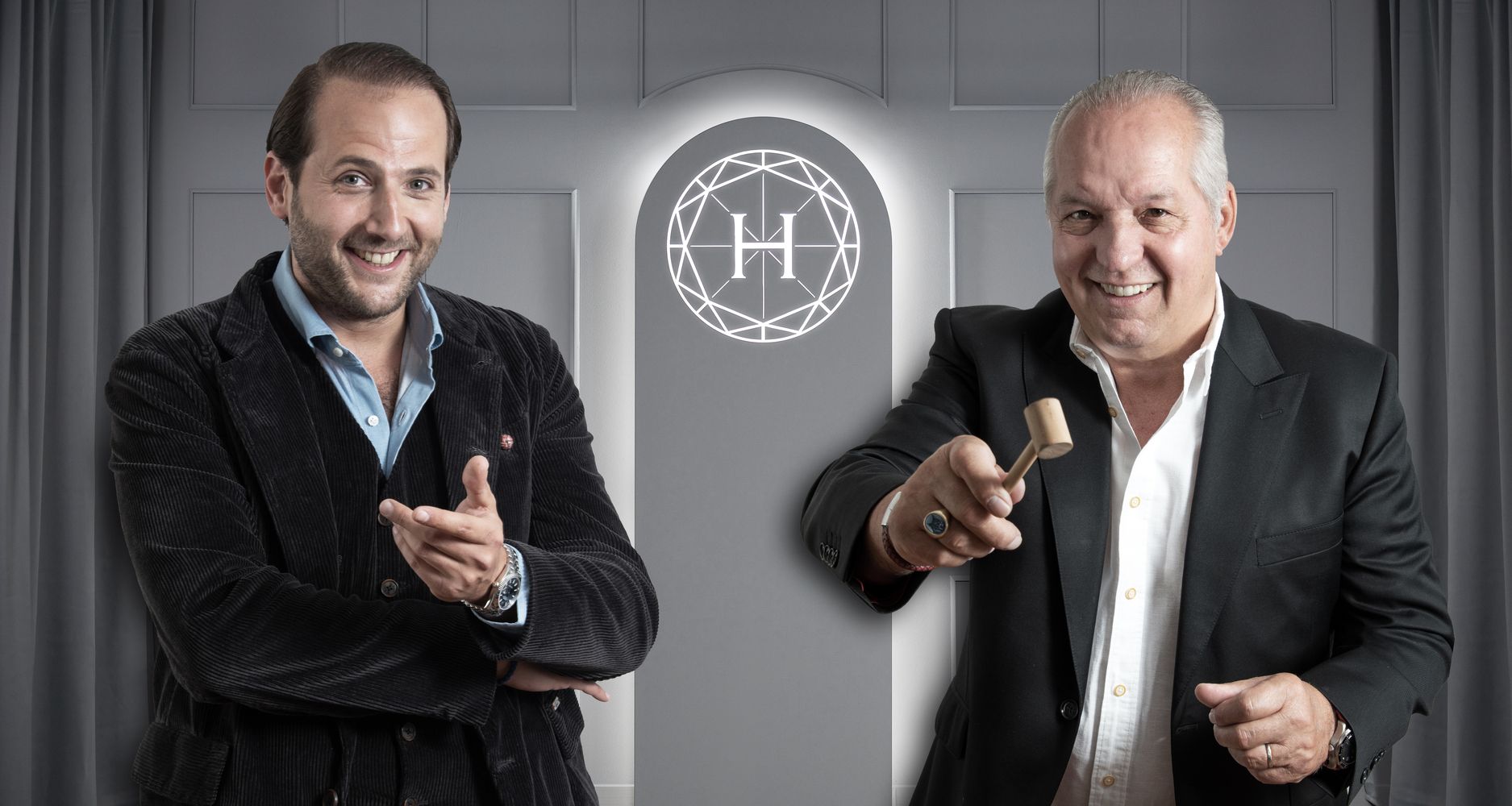 Aufnahme der beiden Auktionatoren vor unserem beleuchteten Logo auf einem strukturierten weißen Hintergrund