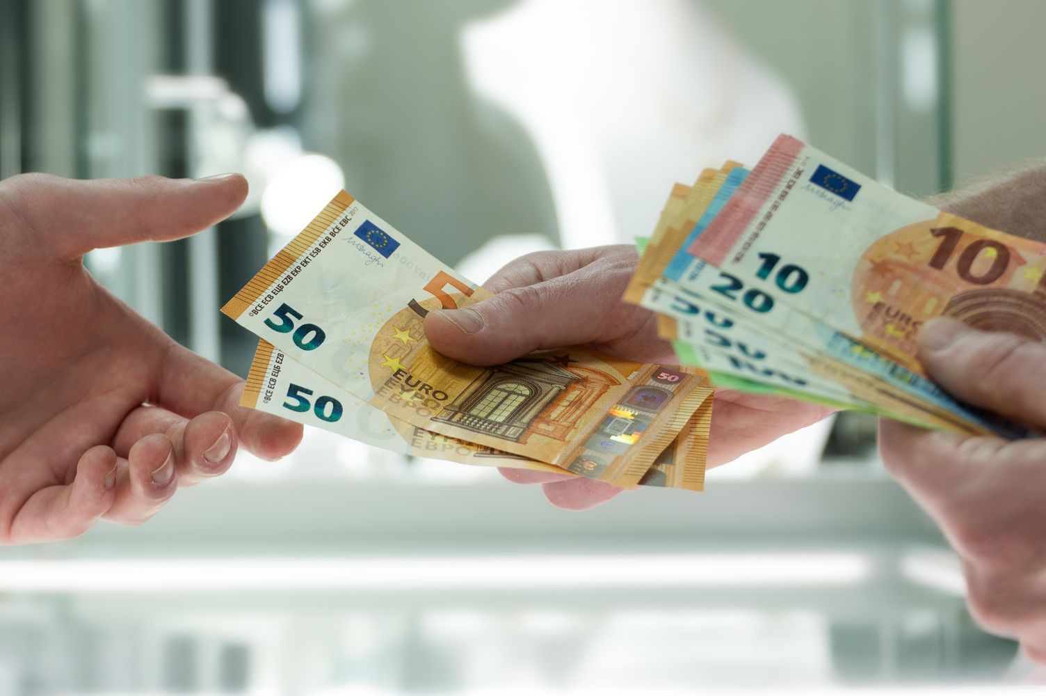 Nahaufnahme zweier Handpaare. Eine Person überreicht der anderen Bargeld.
