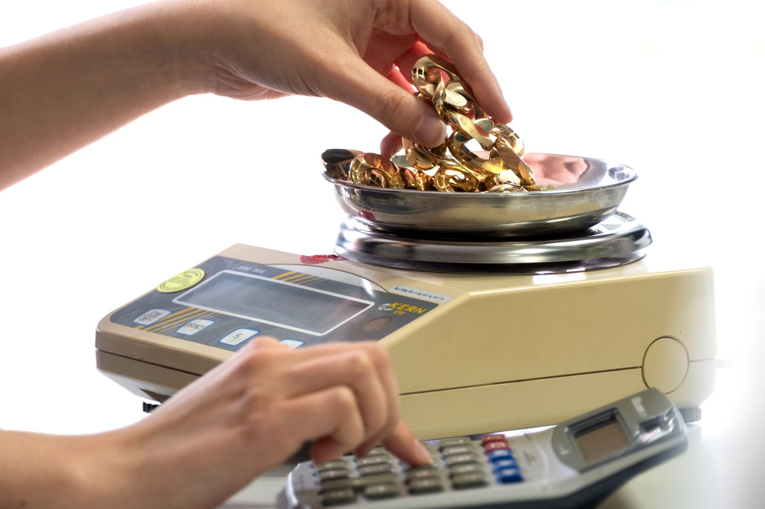 Eine Person wiegt goldfarbene Metallstücke mit einer Waage und berechnet mit einem Taschenrechner deren Wert